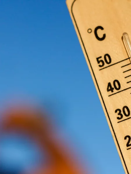 Termomètre qui affiche de hautes température, en fond, un homme boit de l'eau