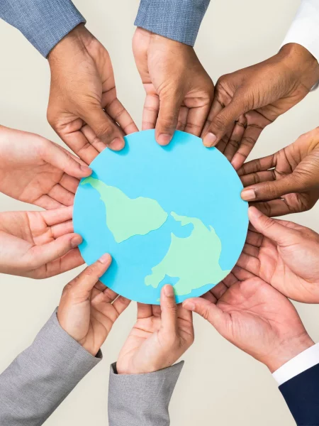 Mains de toutes les couleurs qui tiennent ensemble une planète en papier