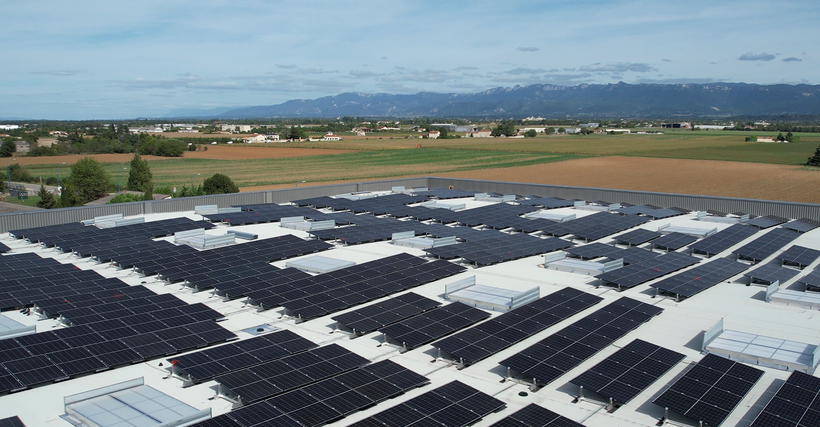 Installation photovoltaïque de grande envergure sur le toit plat d'une entreprise basée dans la zone industrielle de Valence. Le ciel et bleu, il y a des champs et des montagnes au loin.