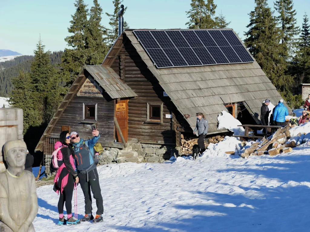 Touristes qui se prennent en photo devant un chalet de montagne sous la neige, équipé de panneaux photovoltaïque