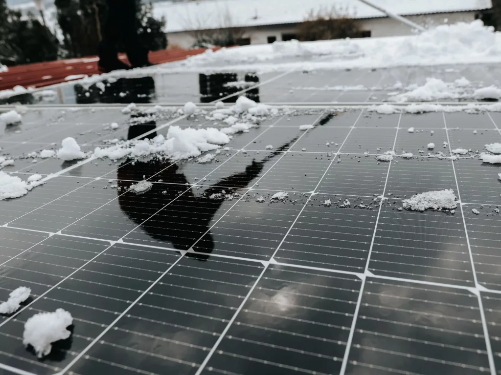 Reflet d'une personne dans un panneau photovoltaïque qui nettoie la neige sur son toit