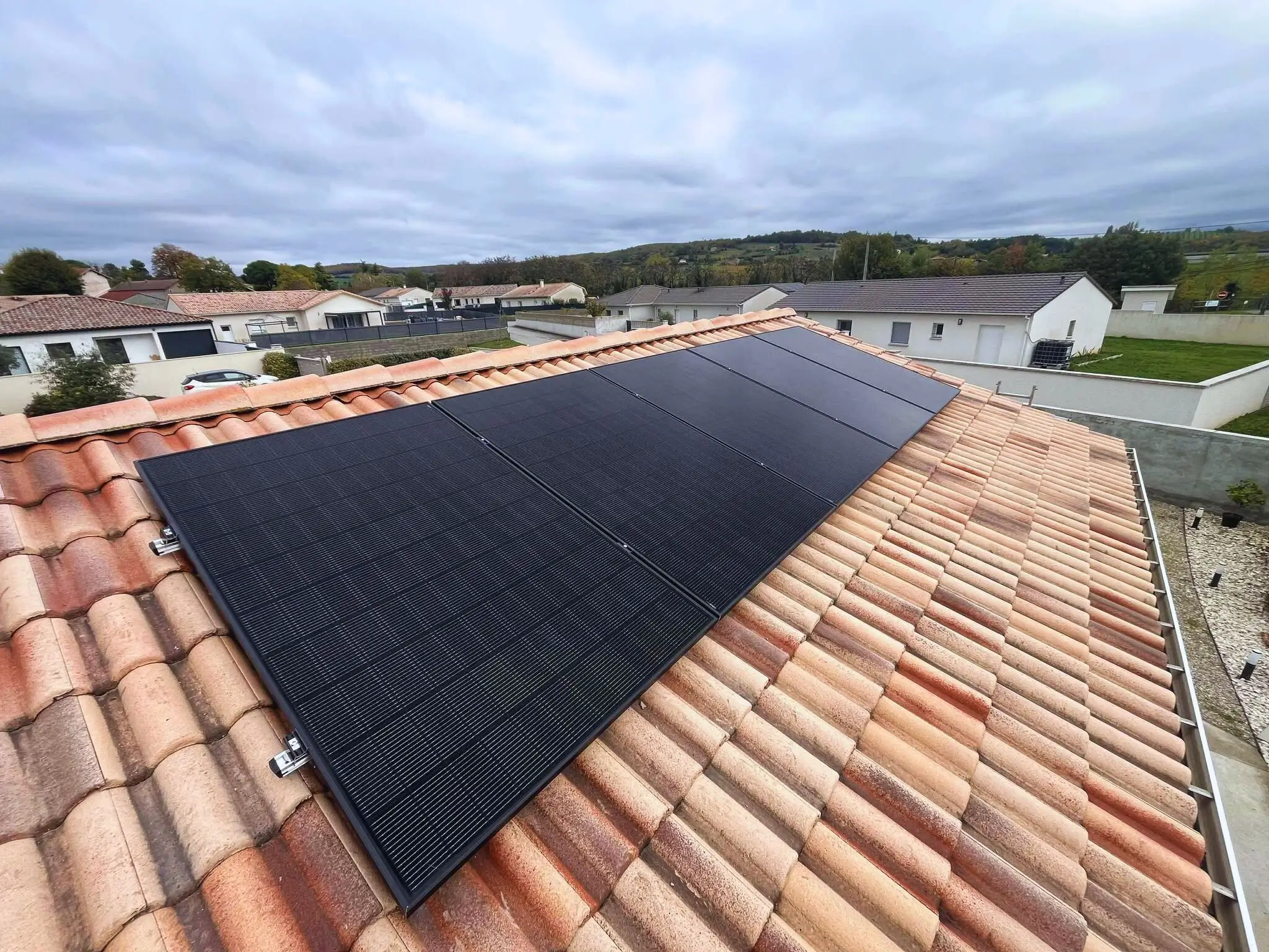 Cinq panneaux photovoltaïques noirs alignés sur la toiture d'une maison individuelle.