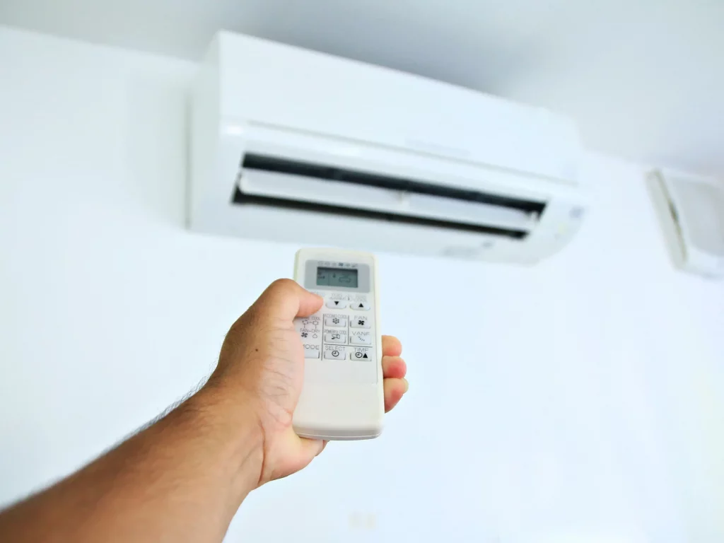 une main dotée d'une télécommande règle la température de la clim réversible