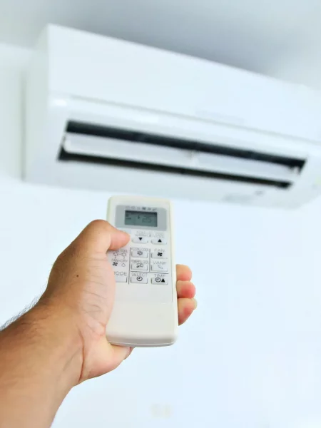 une main dotée d'une télécommande règle la température de la clim réversible