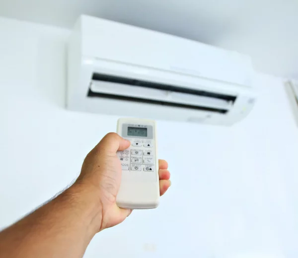 une main dotée d'une télécommande règle la température de la clim réversible